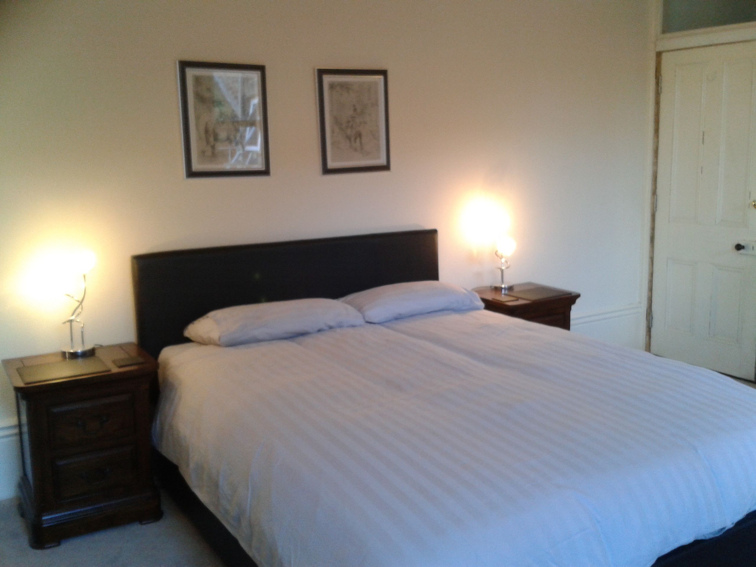A neatly made bed with a headboard, two bedside tables with lamps, and two framed pictures on the wall.
