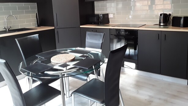 Una cucina moderna con un tavolo rotondo in vetro, sedie nere, un forno nero e mobili grigi.