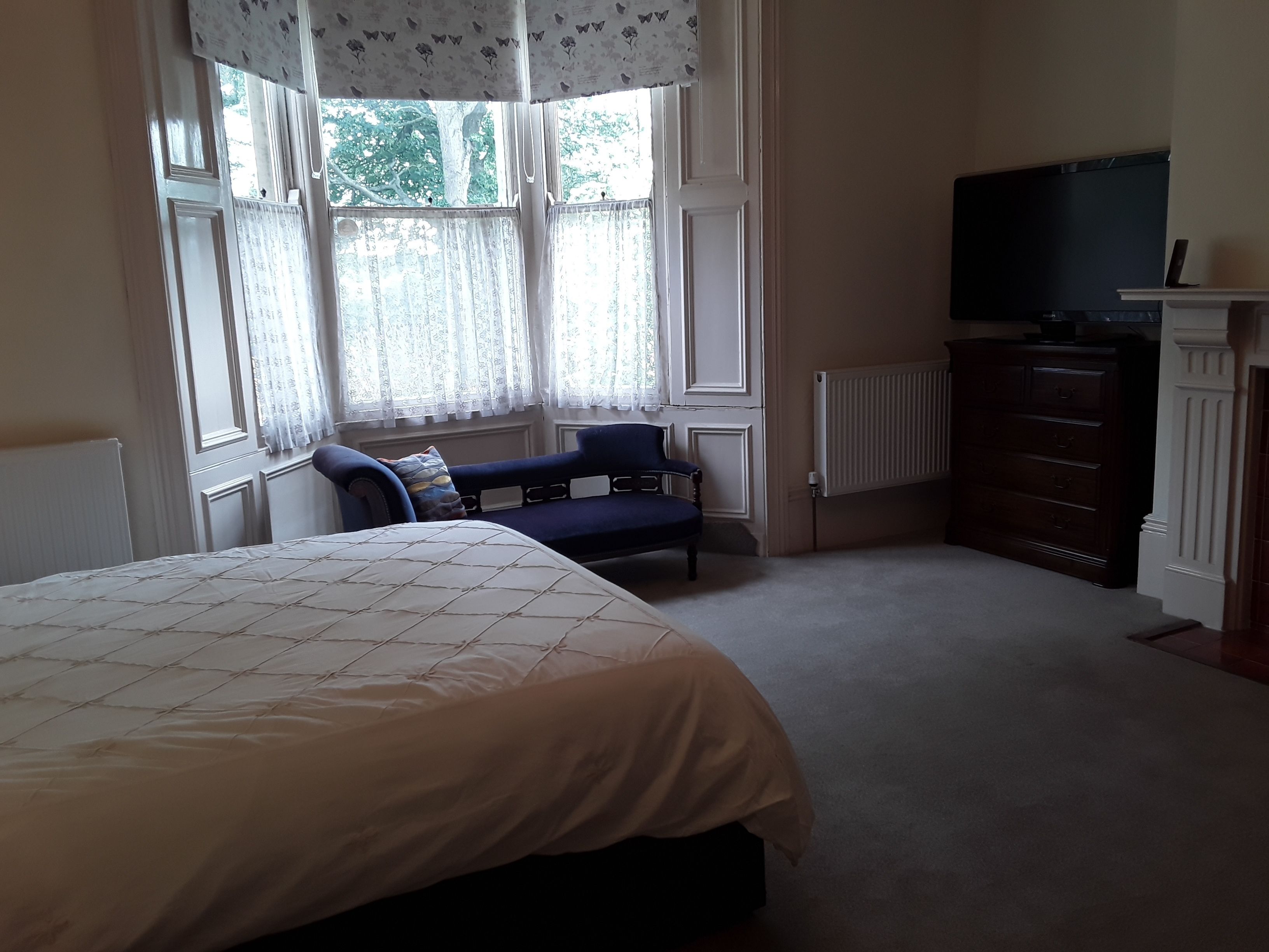 Un dormitorio con una cama grande, un escritorio, una silla, un aparador y un televisor.