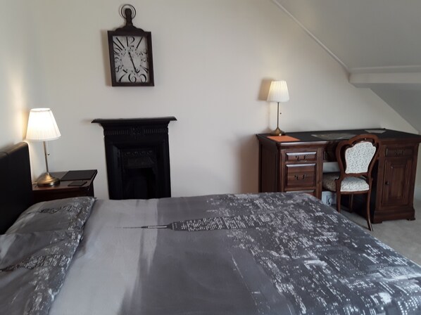 A bedroom with a bed, a fireplace, a desk with a chair, and two lamps. - The Haven (Gateshead)