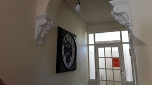 Un corridoio con un orologio grande, una porta con un cartello e un lampadario.