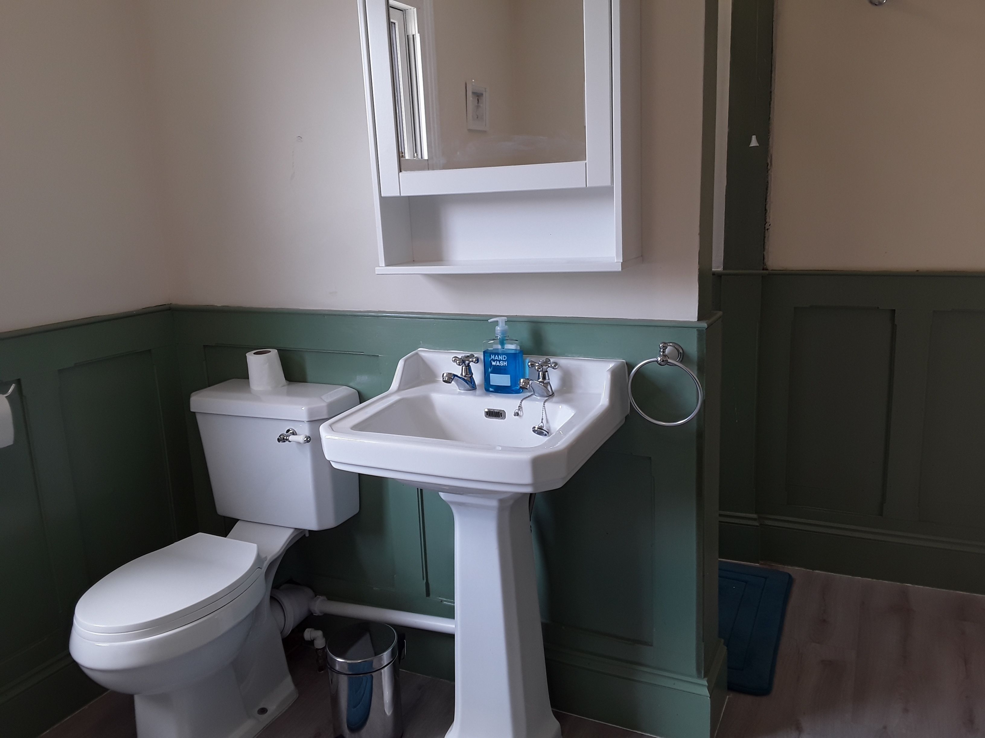A bathroom with a white toilet, a pedestal sink with a soap dispenser, and a towel rack.