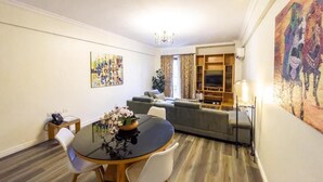 Un coin repas avec une table ronde, des chaises et un vase de fleurs. On aperçoit un canapé et un téléviseur à l’arrière-plan.