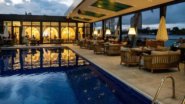 Un espace aménagé au bord de la piscine, avec des chaises longues et des tables, une piscine, et une vue sur les gratte-ciel de la ville.
