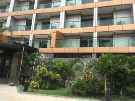 Un edificio de varios pisos con balcones, fachada de piedra y exuberante vegetación al frente.