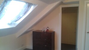 A room with a sloped ceiling, a small wooden dresser, and a door leading to another room. - Avenue Road (Gateshead)