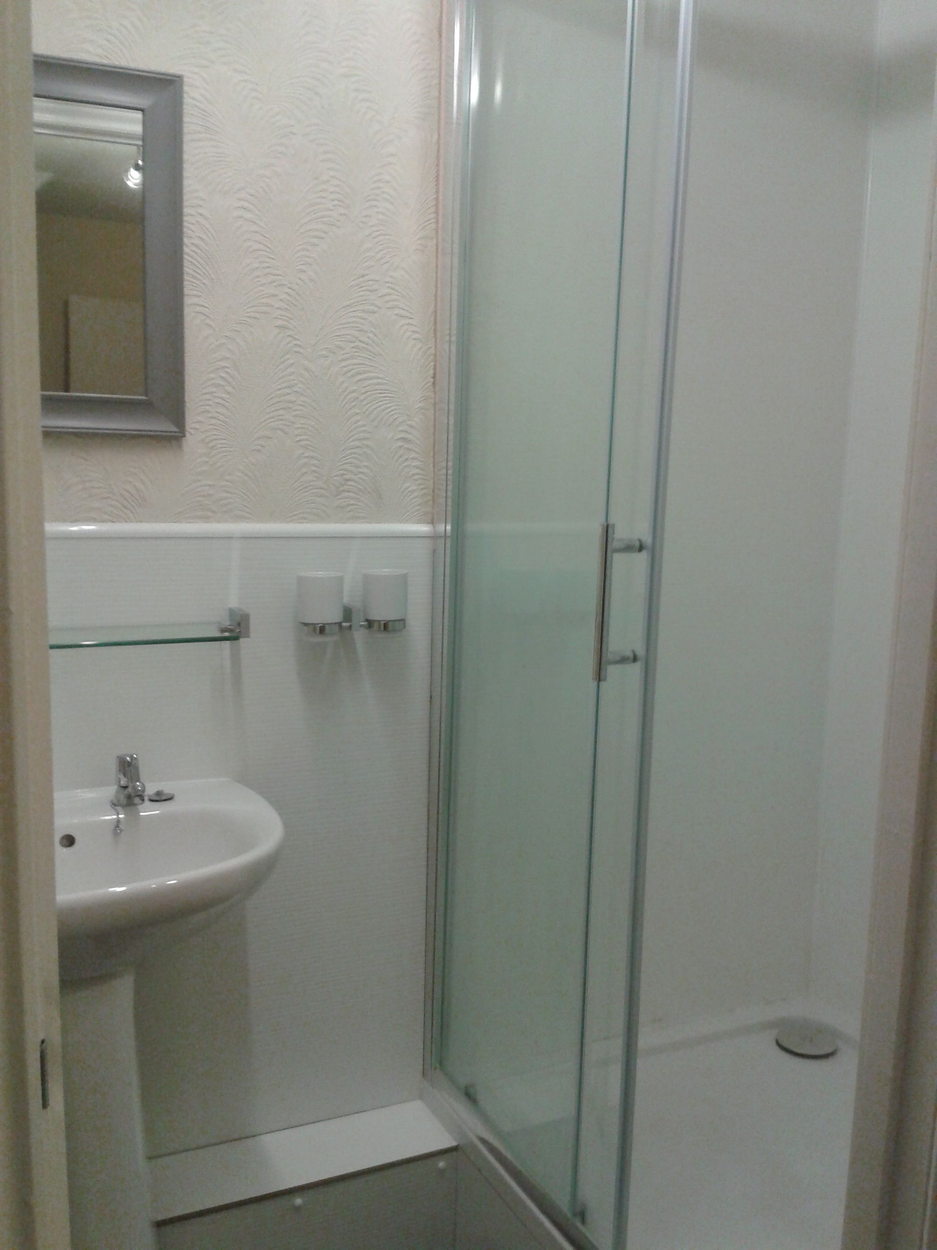 A bathroom with a glass-enclosed shower, a sink, and two soap dispensers on the wall.
