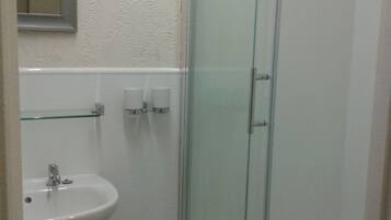 A bathroom with a glass-enclosed shower, a sink, and two soap dispensers on the wall.
