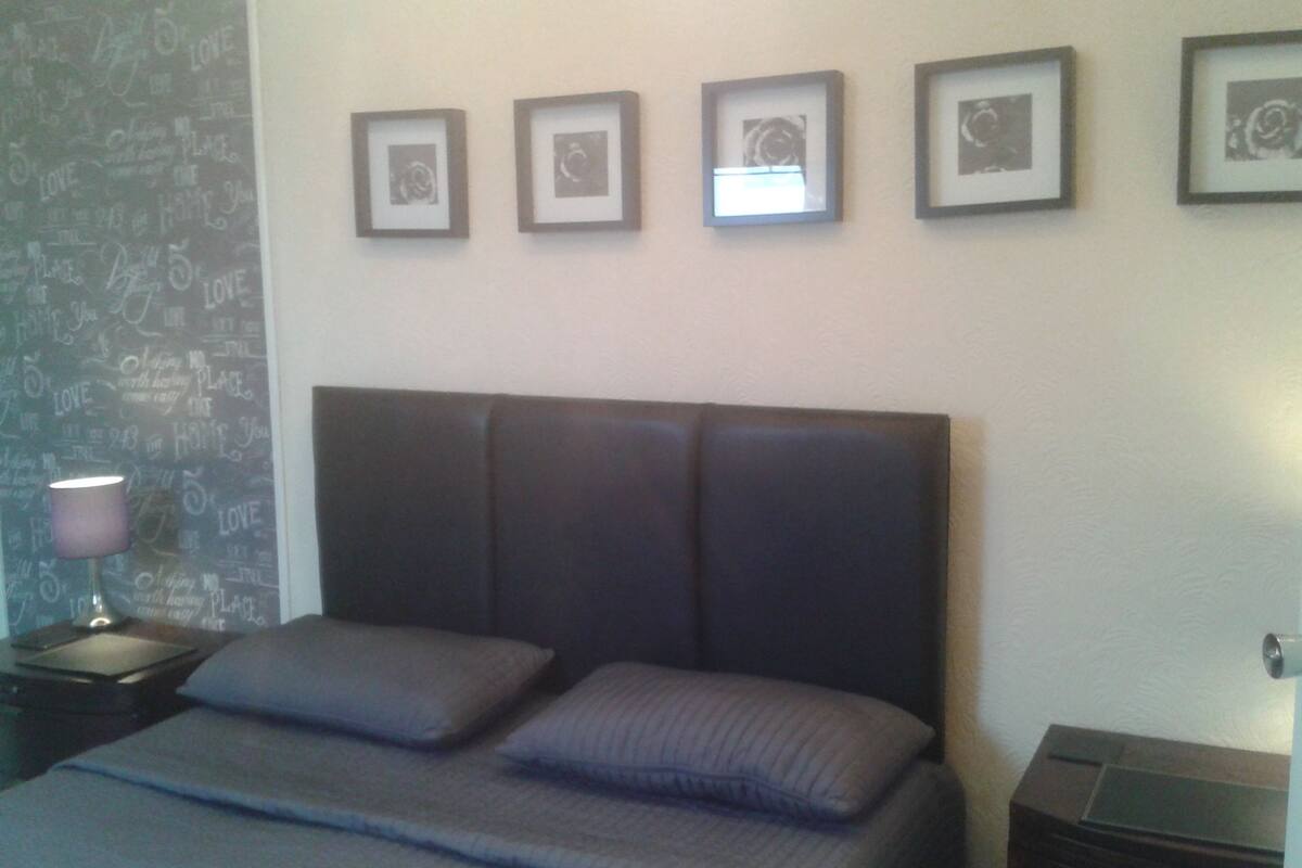 Ein Schlafzimmer mit einem großen Bett, einem Nachttisch mit Lampe und vier gerahmten Bildern an der Wand.