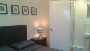 A bedroom with a bed, a nightstand with a lamp, a door, and a bathroom with a sink. - Avenue Road (Gateshead)