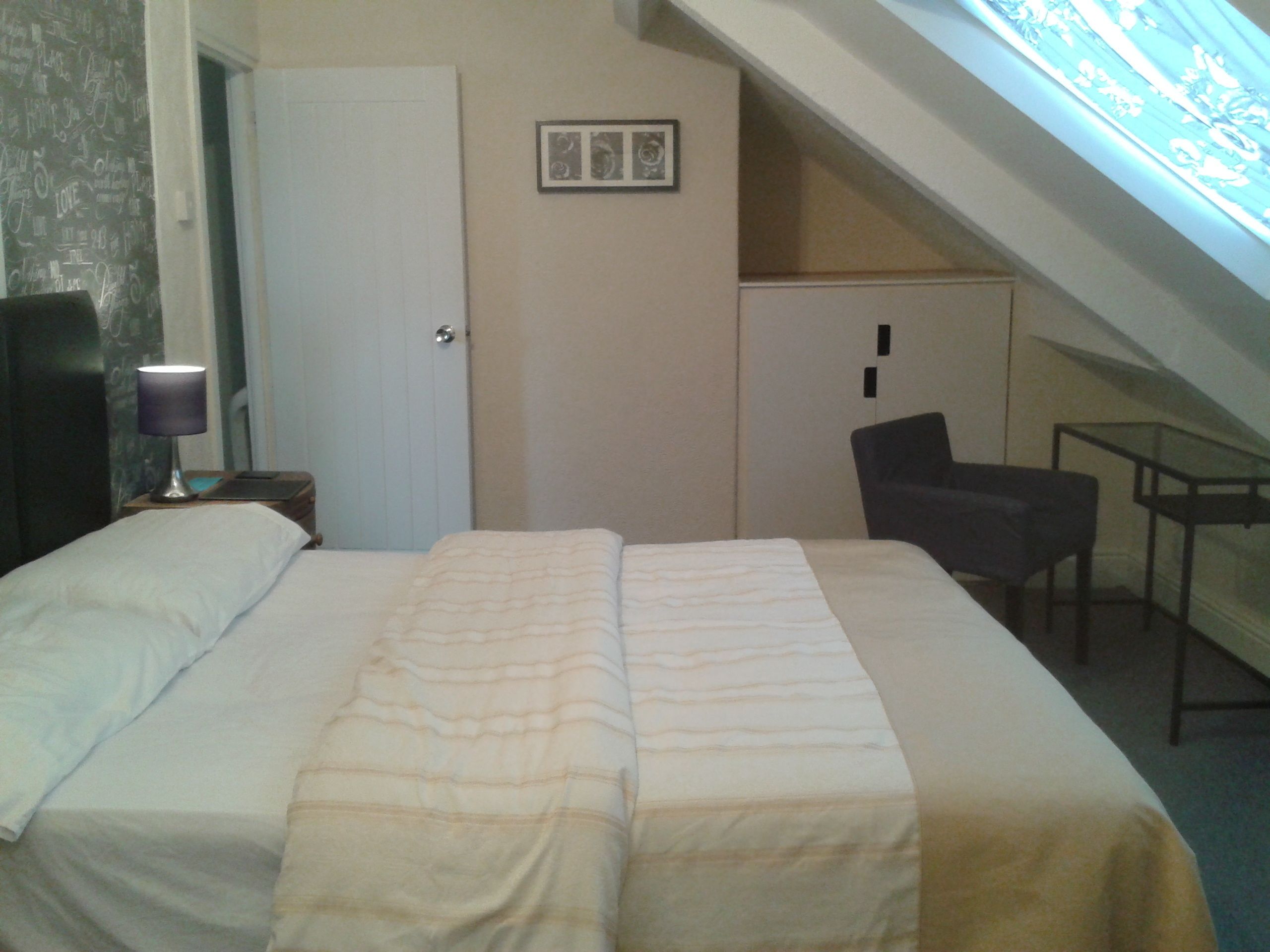 Un dormitorio con cama, escritorio, silla y tragaluz.