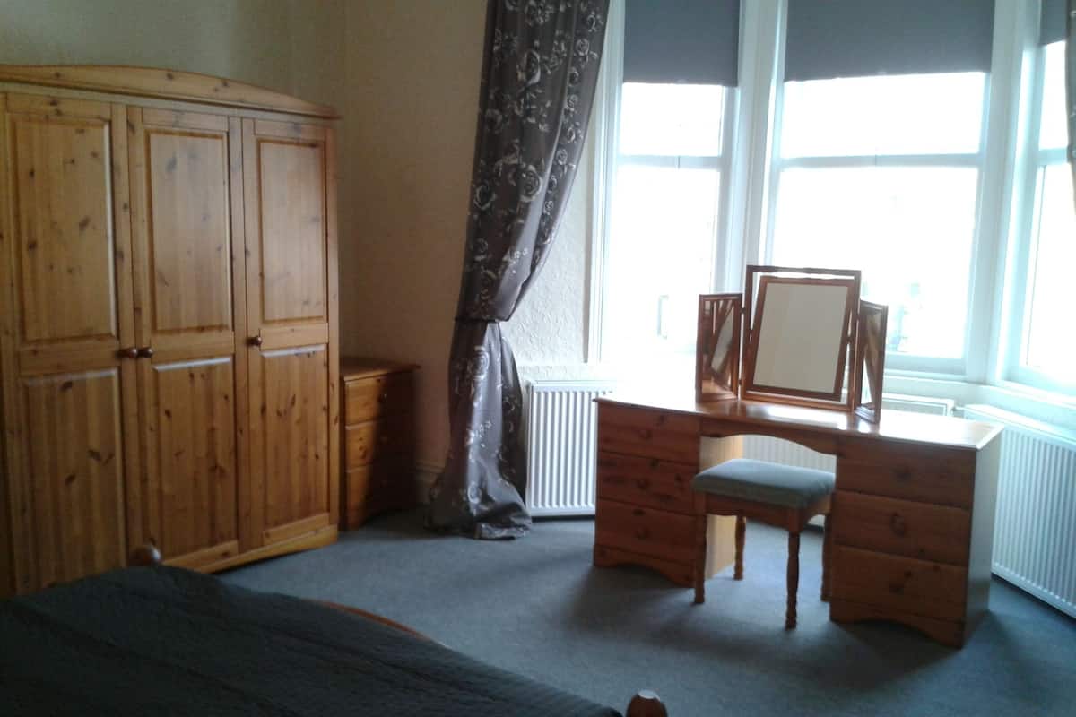 Ein Schlafzimmer mit einem Bett, einem Holzschrank, einem Schreibtisch mit Stuhl und einem Fenster mit Vorhängen.