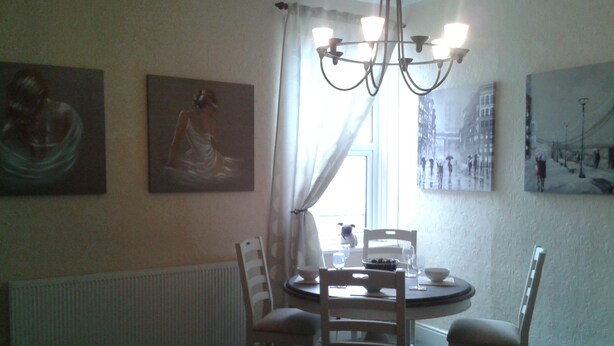 A dining area with a round table, four chairs, a chandelier, and artwork on the walls. - Avenue Road (Gateshead)