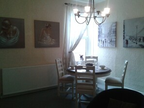 A dining area with a round table, four chairs, a chandelier, and artwork on the walls. - Avenue Road (Gateshead)