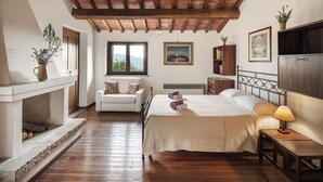 A bedroom with a bed, a chair, a fireplace, a window, and a TV. - Villa Lavanda Todi, countryside casale with private pool in the heart of Umbria (Canonica, PG)