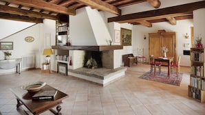 A spacious living room with exposed wooden beams, a fireplace, a dining area with chairs, and a bookshelf. - Villa Lavanda Todi, countryside casale with private pool in the heart of Umbria (Canonica, PG)