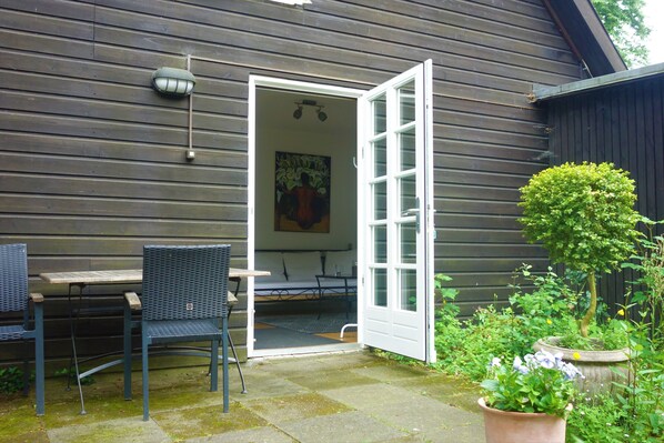 An open door leading to a room with a table and chairs, a painting on the wall, and a potted plant outside. - Ferienwohnung Katharina (Undeloh)