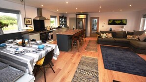 Une cuisine moderne avec un îlot central, un coin repas avec une nappe à rayures et un salon doté d’un canapé foncé.