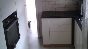 Una cocina con armarios blancos, encimera negra y salpicadero de azulejos. Hay un cuadro en la pared y una puerta que da a otra habitación.