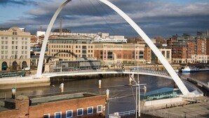 Un puente moderno con un arco blanco que cruza un río, rodeado de edificios urbanos.