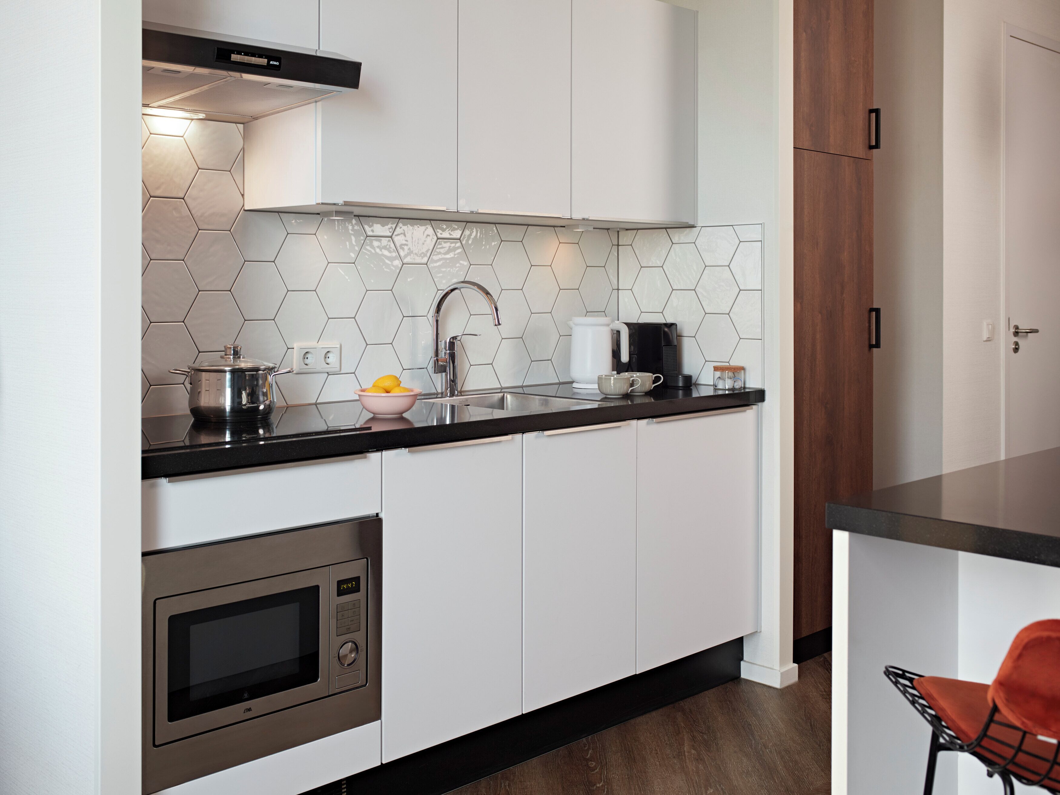 Une cuisine moderne avec des meubles blancs, un plan de travail noir, un four en acier inoxydable et un dosseret de carrelage hexagonal.