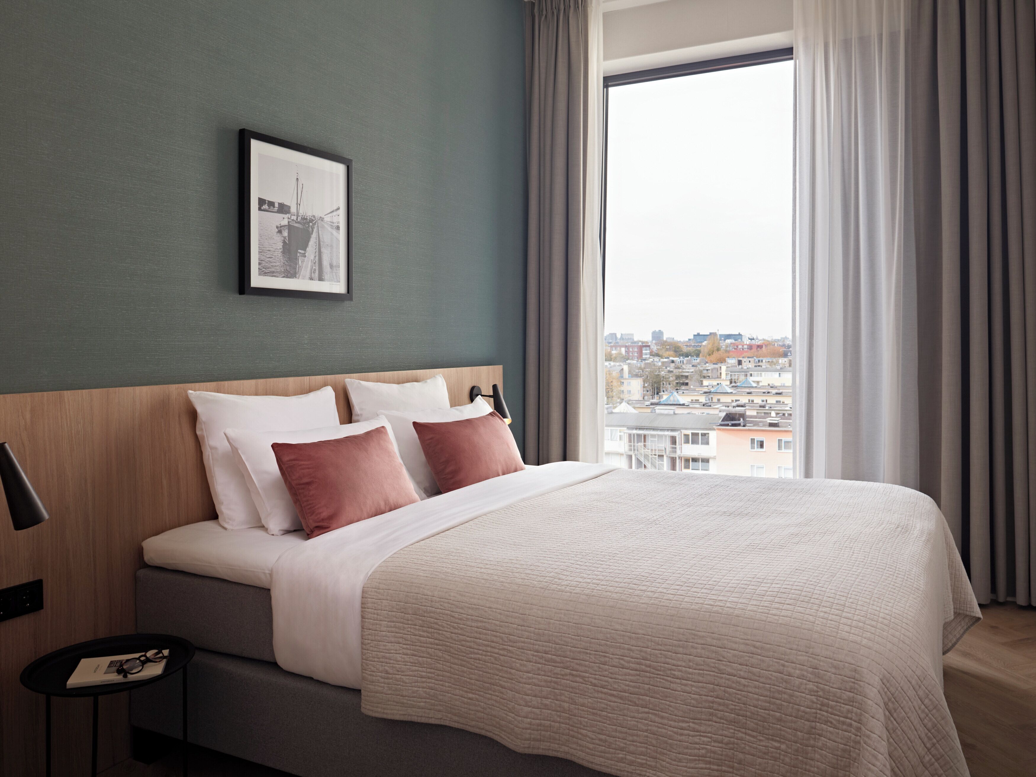 Et moderne hotelværelse med en stor seng, udsigt over byen og et billede i ramme på væggen.