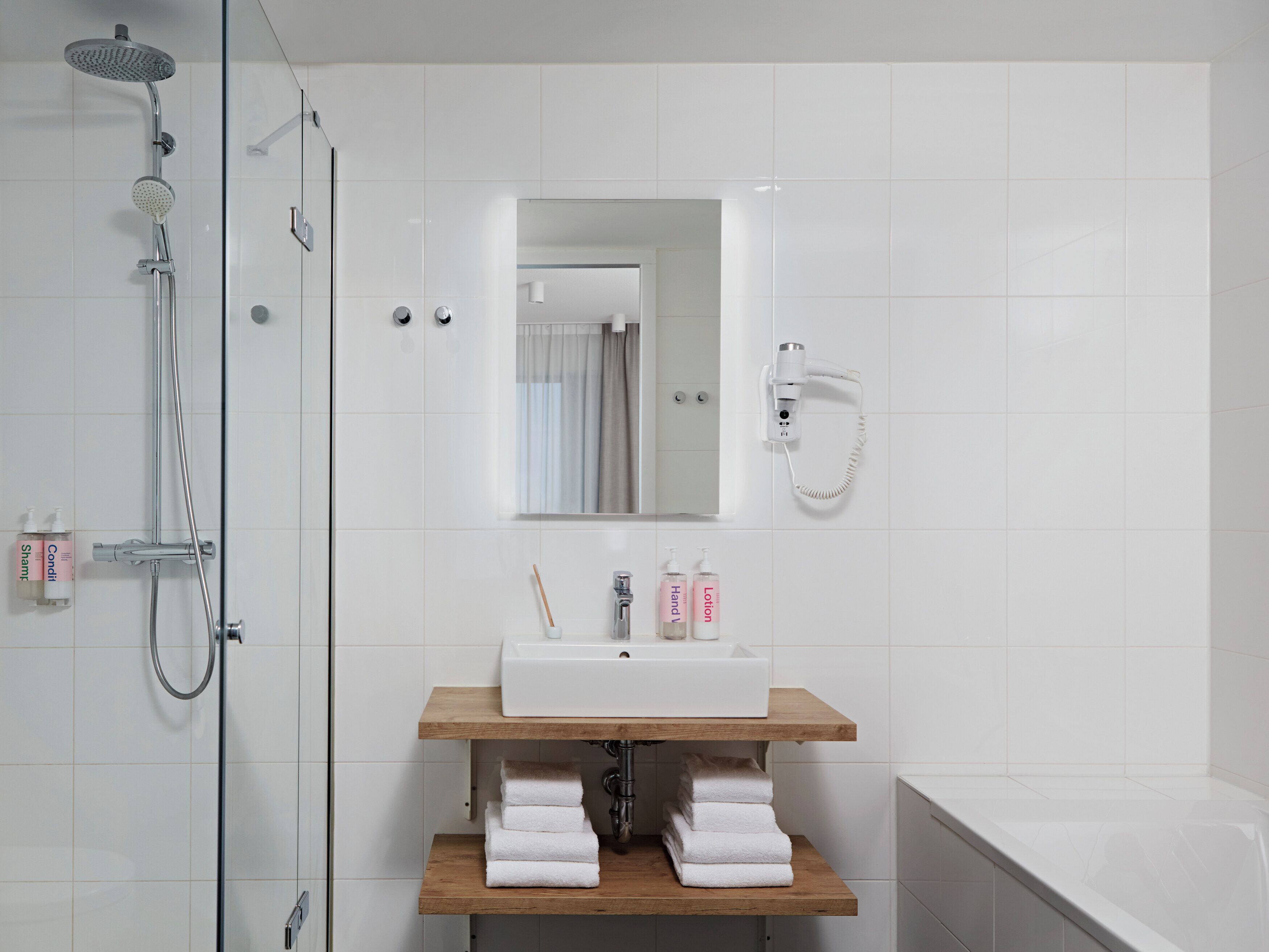 A modern bathroom with a glass-enclosed shower, a white sink with a wooden shelf, and a white bathtub.