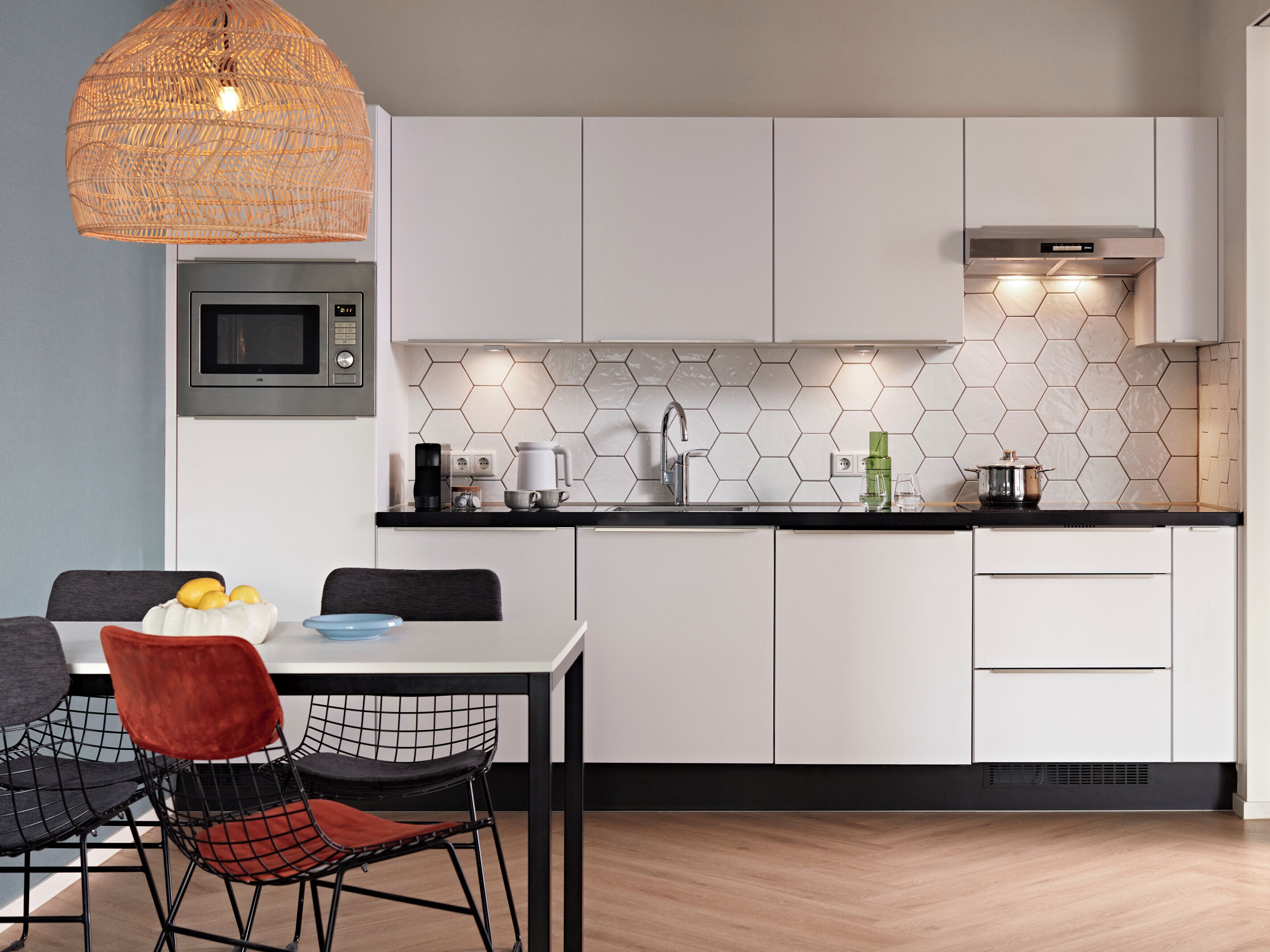 Una cocina moderna con armarios blancos, encimera negra, microondas, cafetera y una lámpara colgante.
