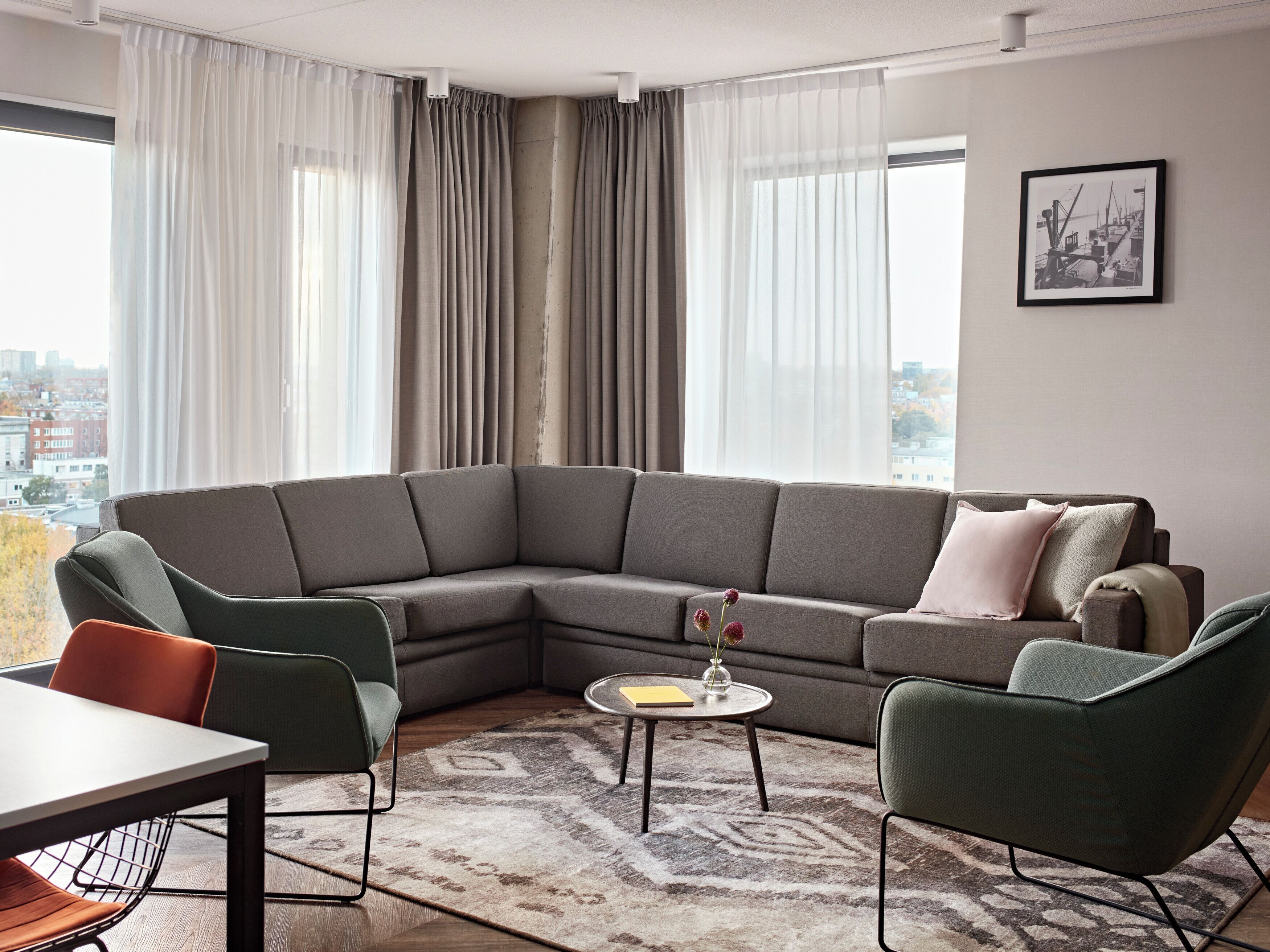 A modern living room with a sectional sofa, two armchairs, a small round table, and a dining table with chairs.