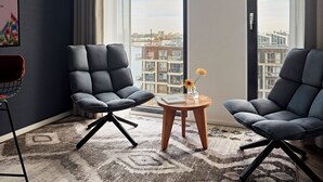 A modern living room with two grey armchairs, a small wooden table, and a large window offering a city view. - Numa Amsterdam Docklands (Amsterdam)
