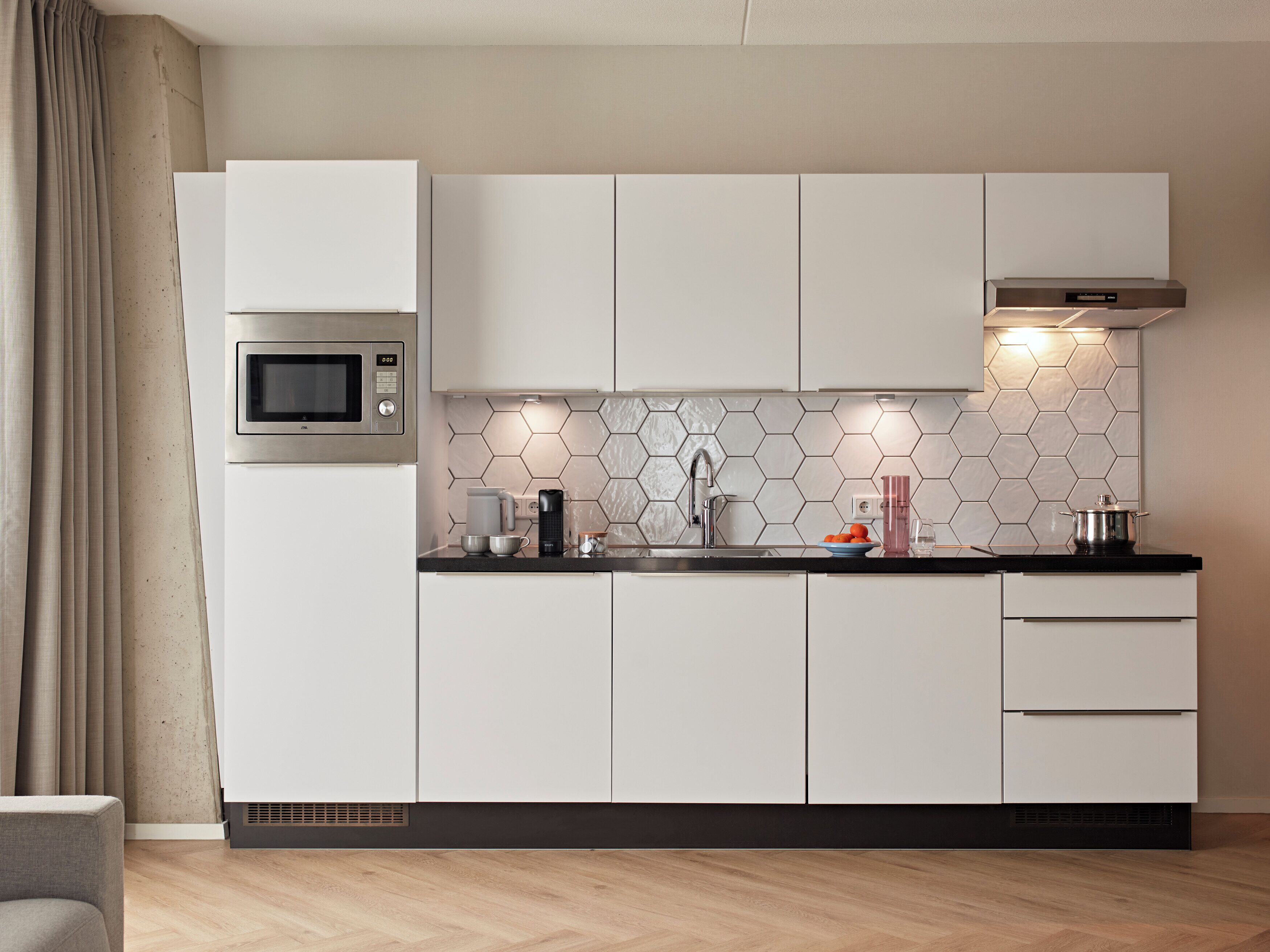 Una cocina moderna con armarios blancos, microondas, fregadero y salpicadero de azulejos hexagonales.
