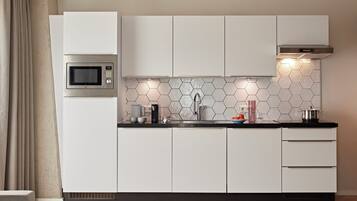 Una cocina moderna con armarios blancos, microondas, fregadero y salpicadero de azulejos hexagonales.