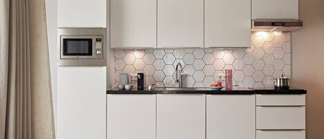 Una cocina moderna con armarios blancos, microondas, fregadero y salpicadero de azulejos hexagonales.