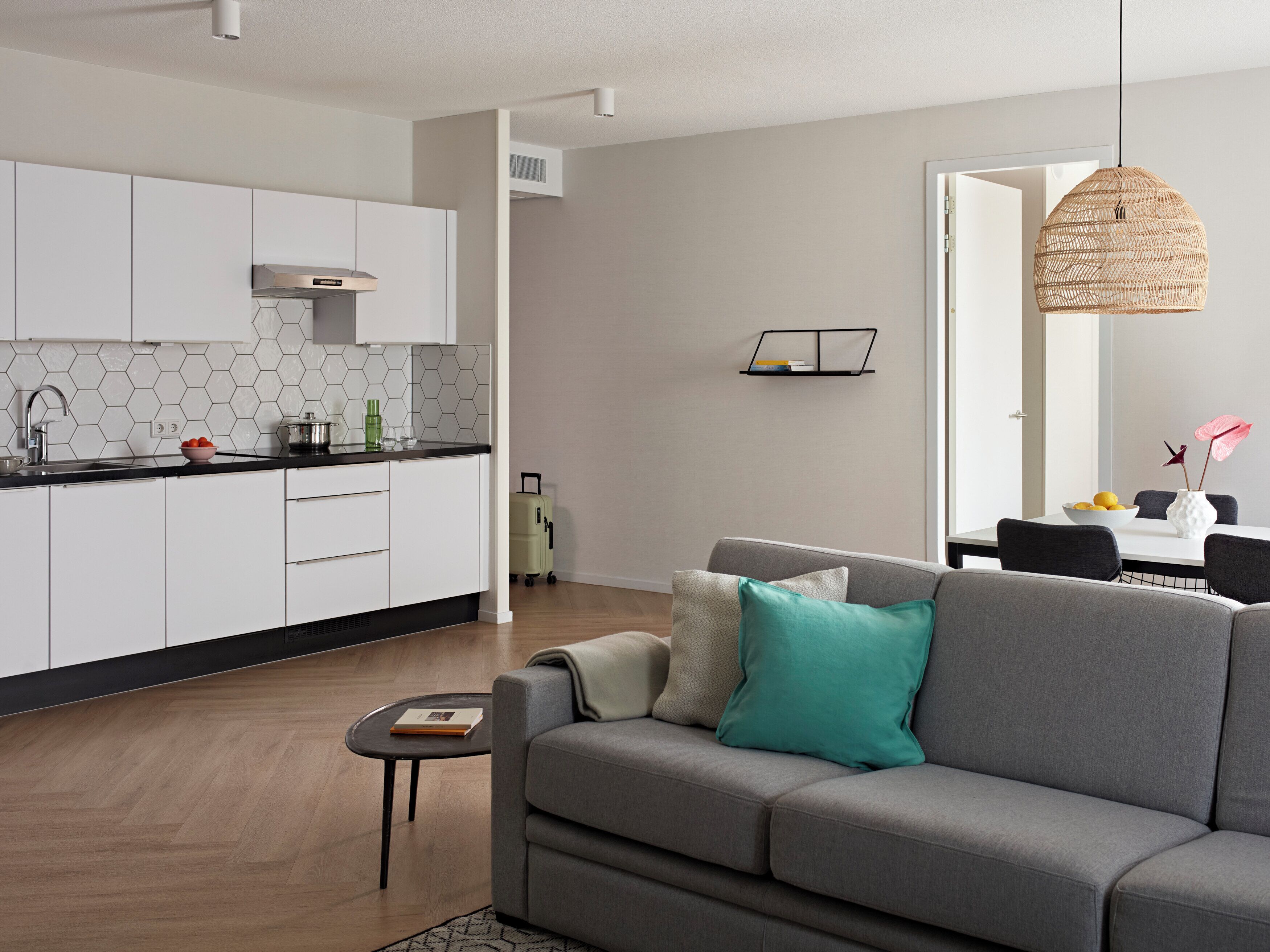 A modern living room with a grey sofa, a small coffee table, and a kitchen area with white cabinets and a black countertop.