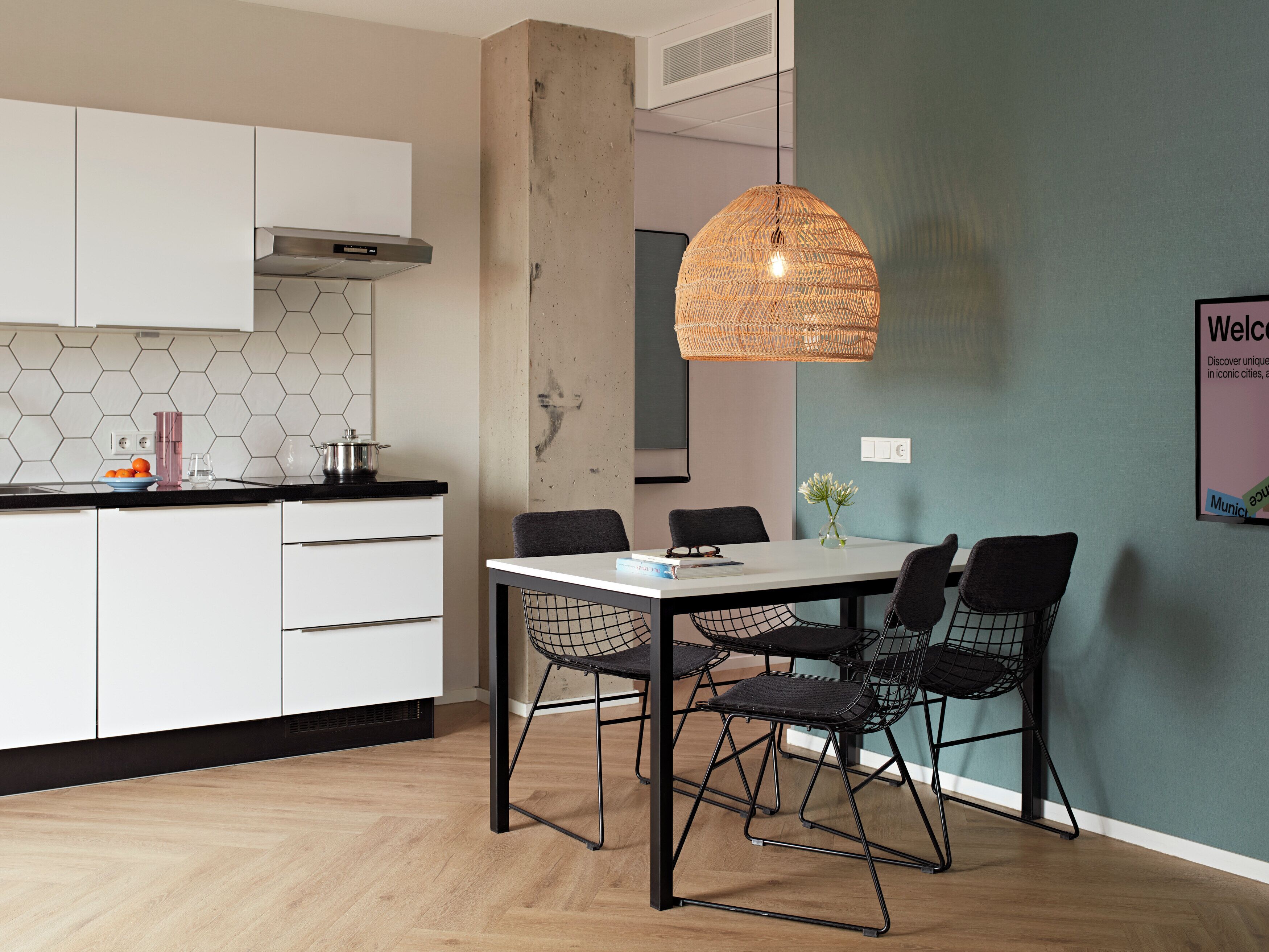 A modern kitchen with white cabinets, a hexagonal backsplash, and a dining area with a white table and black wireframe chairs.