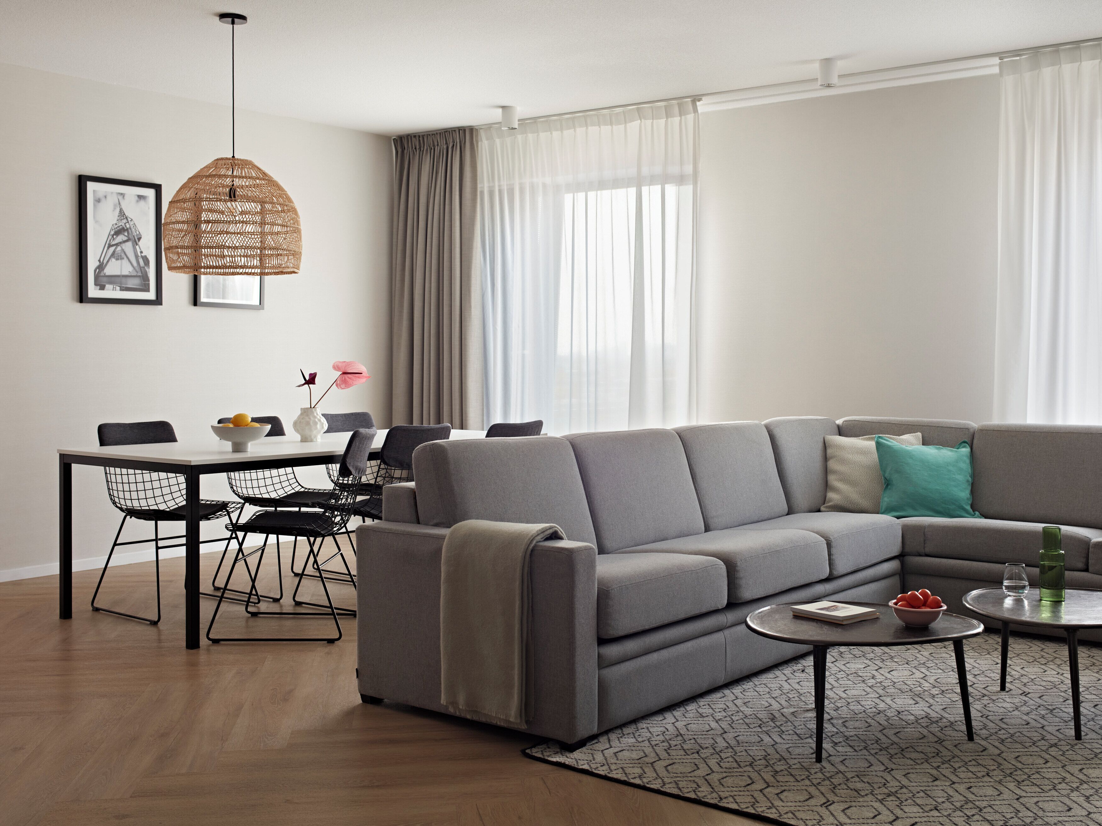 A modern living room with a grey sectional sofa, a dining table with chairs, a hanging light fixture, and a patterned rug.
