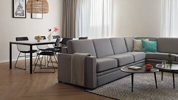 A modern living room with a grey sectional sofa, a dining table with chairs, a hanging light fixture, and a patterned rug.