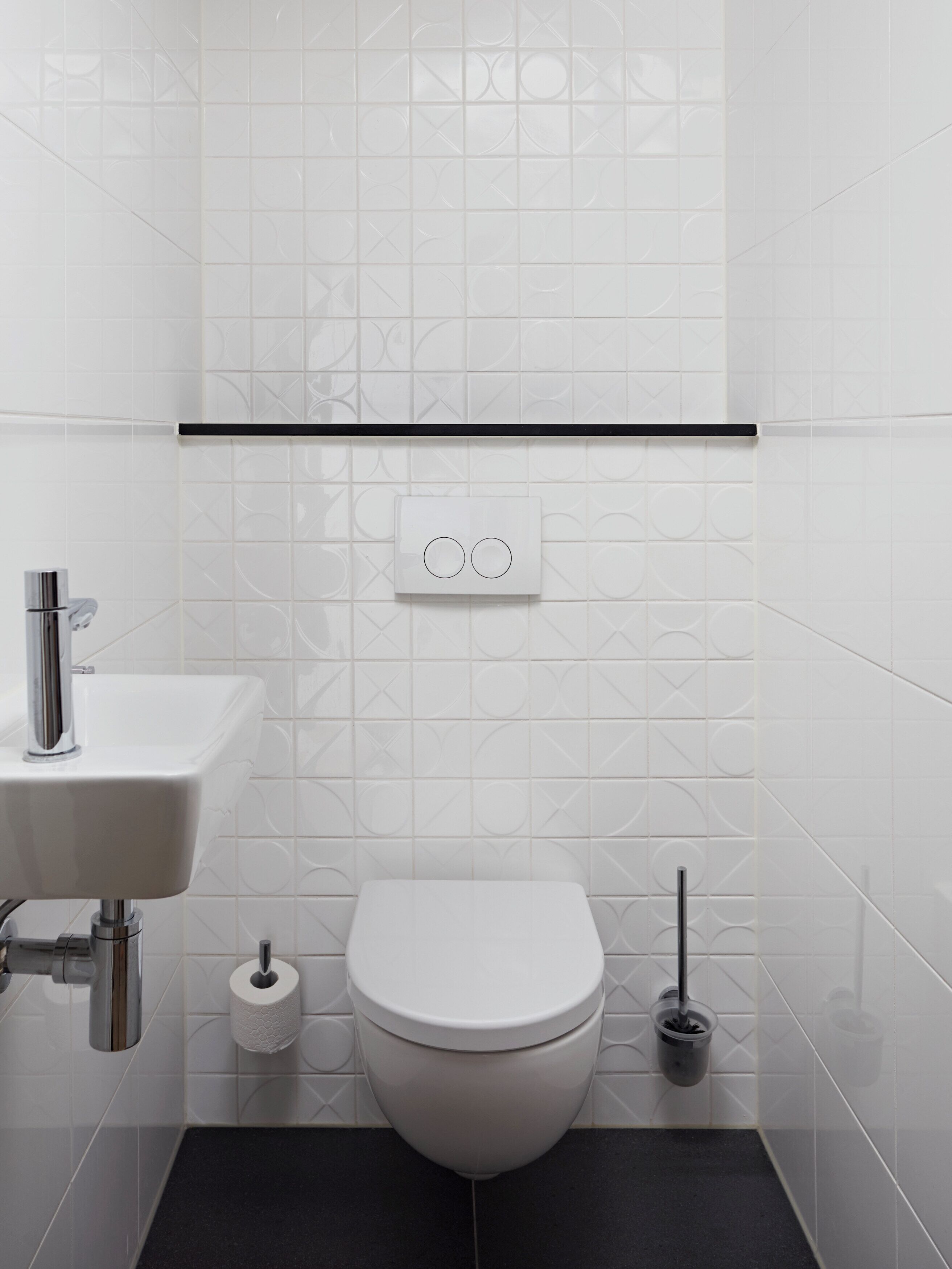 A modern bathroom with a white toilet, a sink, and a toilet paper holder.