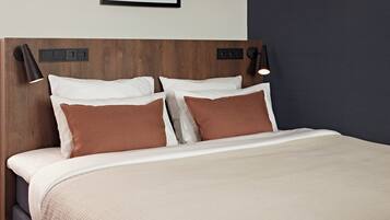 A neatly made bed with a beige quilt, two white pillows, and two brown pillows. There are two black wall-mounted lamps on either side of the bed.