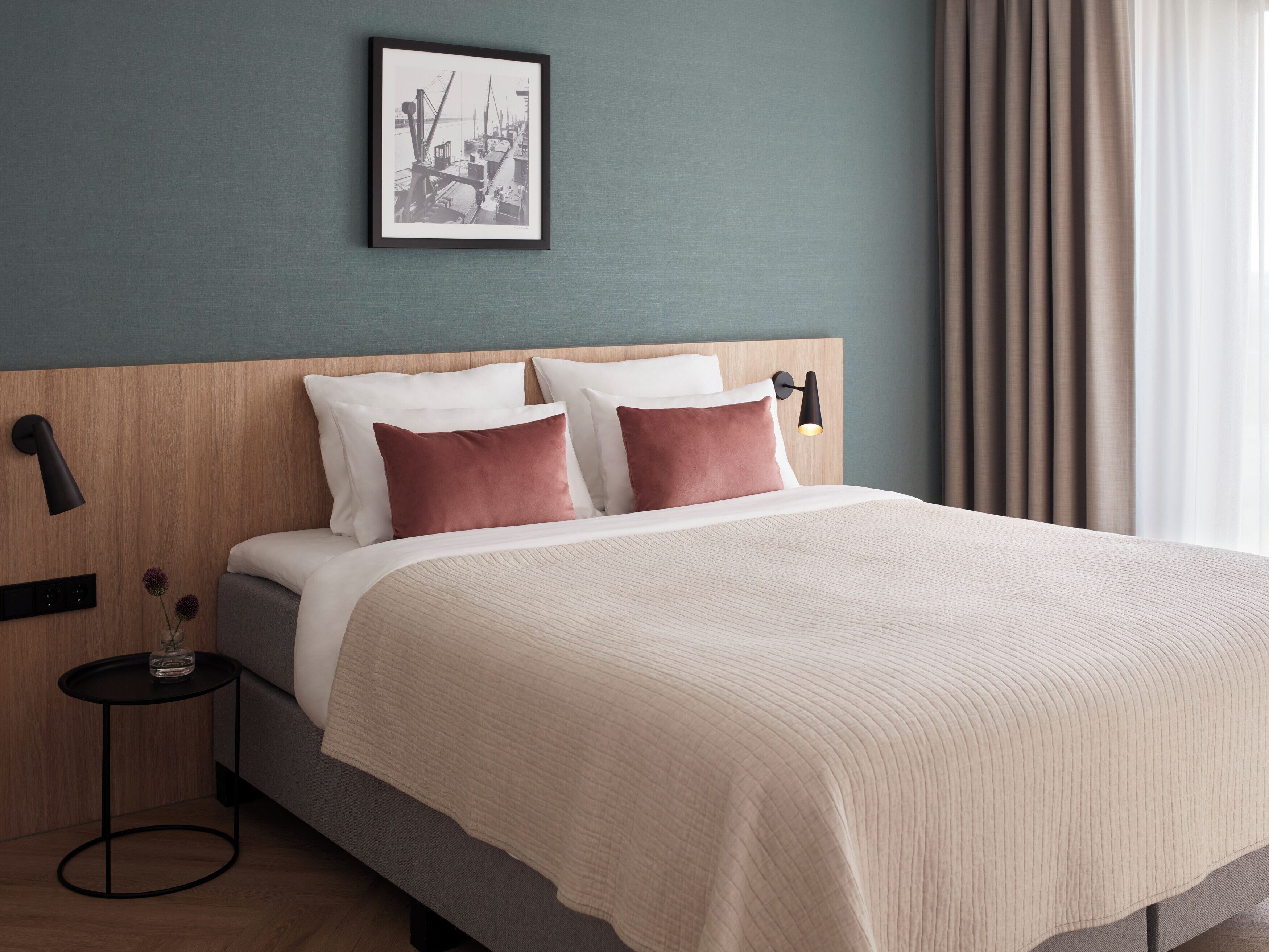 A neatly made bed with a beige quilt, two pillows, and a framed picture on the wall.