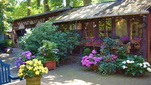 A wooden outdoor seating area with a table and chairs, surrounded by potted plants and flowers. - Ferienwohnung Eichhof (Garlstorf am Walde)
