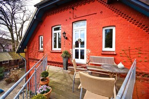 Una casa de ladrillo rojo con un balcón, muebles de mimbre y plantas en macetas.