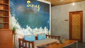 A room with a wooden sofa, a wooden table, and a wall with a wave painting. - Sinag Hostel - Adults Only (General Luna)