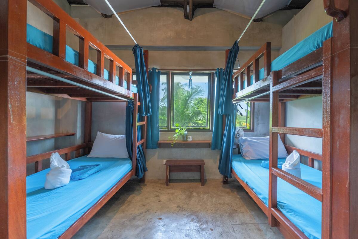 A room with bunk beds, a small bench, and a window with curtains.