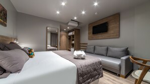 A modern hotel room with a bed, a sofa, a TV mounted on the wall, and a wooden floor. - Hotel Laghetto Fratello (Gramado)