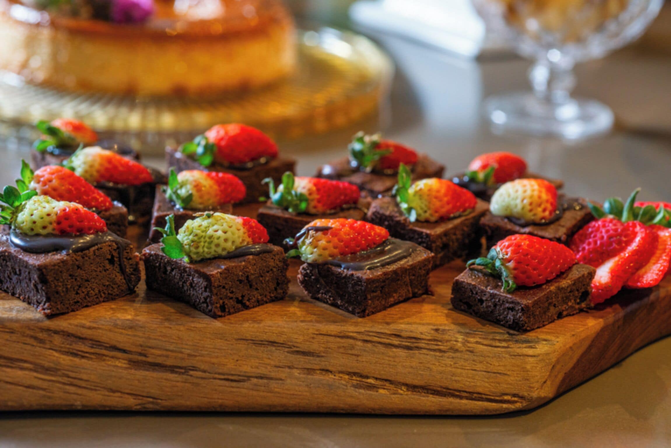 Une planche en bois sur laquelle sont disposés plusieurs carrés de brownie, garnis de fraises et de feuilles de menthe.