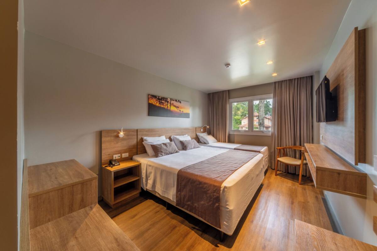 A modern hotel room with a large bed, wooden headboard, bedside tables, a desk, and a TV mounted on the wall.