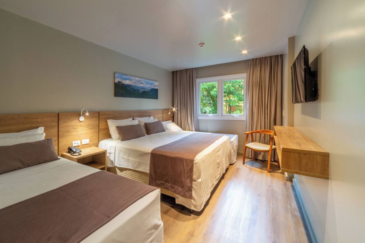 A hotel room with two beds, a desk, a chair, a TV, and a window with curtains.