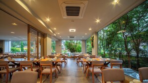 A spacious restaurant with multiple tables and chairs, large windows offering a view of greenery outside, and a ceiling with recessed lighting. - Hotel Laghetto Fratello (Gramado)