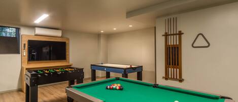A room with a pool table, a foosball table, and a television.